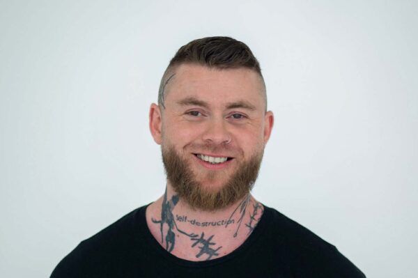 Juri Orlov. Mann mit kurzem Harrschnitt, einem Vollbart, Tatowierungen am Hals und  in einem schwarzem Shirt.